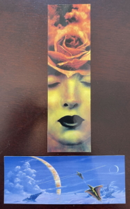 Two bookmarks, one depicting a rose emerging from a woman’s forehead, the other depicting a fantasy space scene with dragons and spaceships.