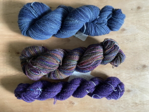 Three skeins of handspun yarn in blue and jewel tones.