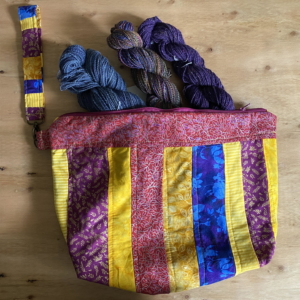 A handmade project bag containing three skeins of handspun yarn.